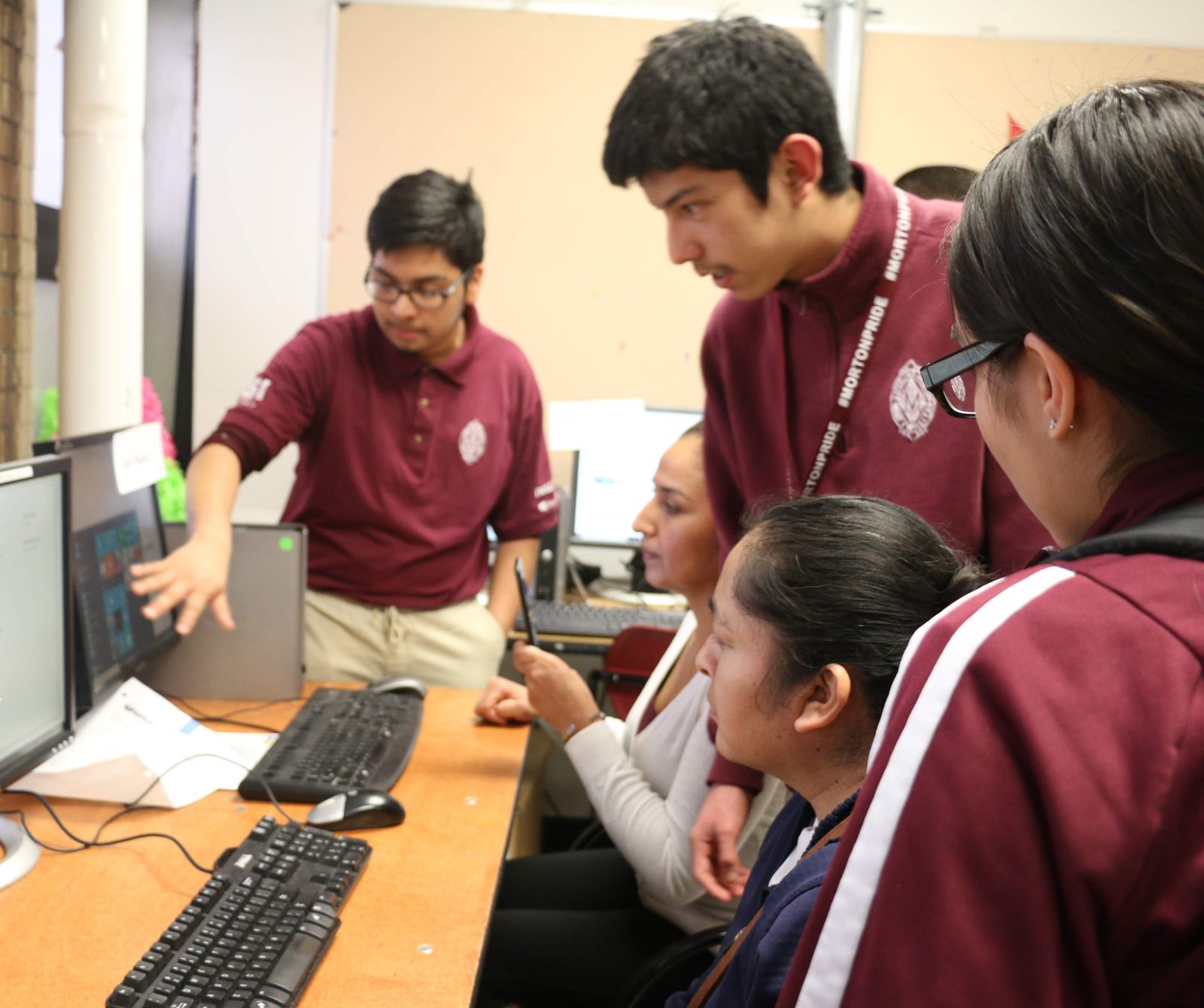 Morton East students in maroon polos around a monitor, one explaining something to the others